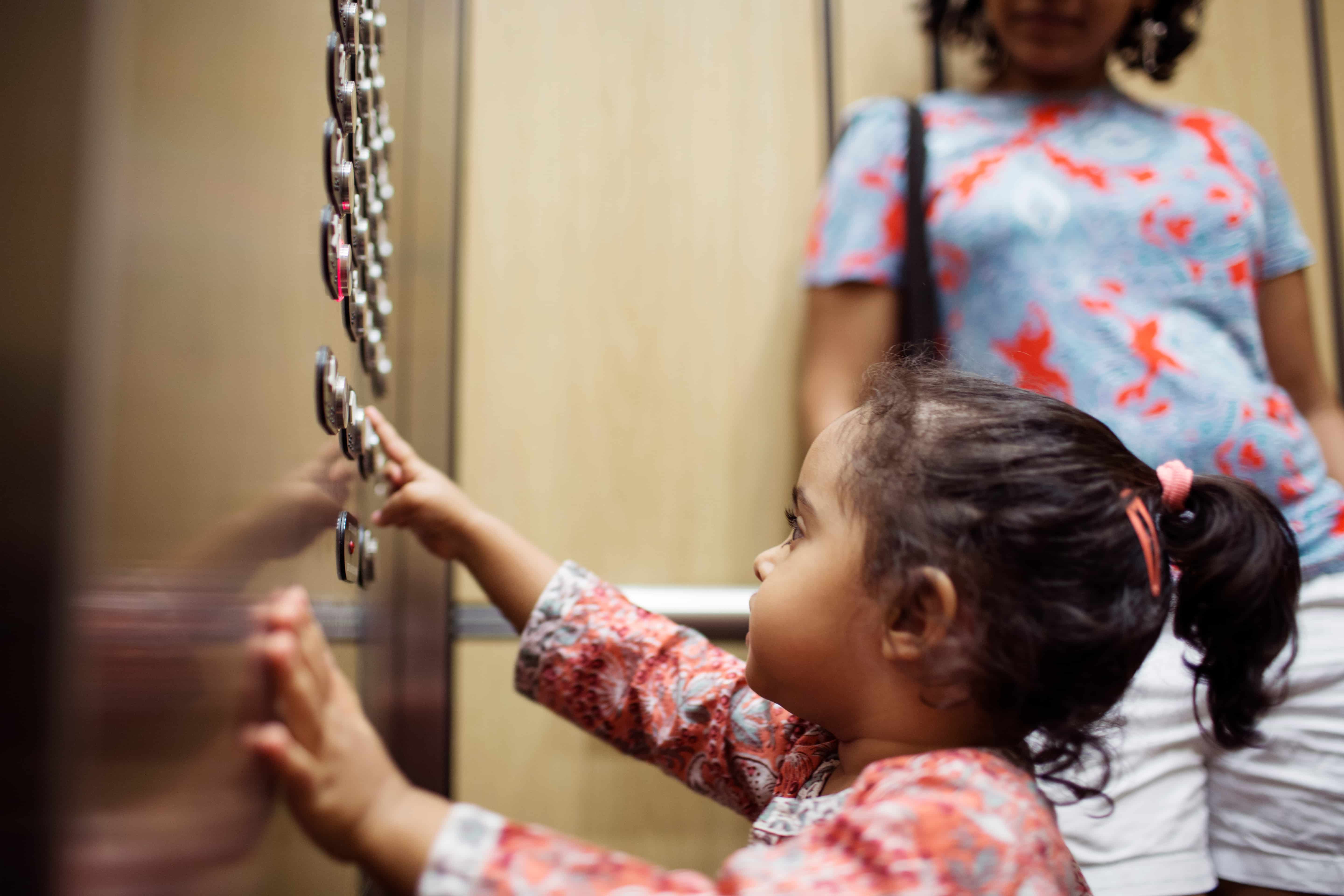 Girl pushing push button while standing by mother in elevator