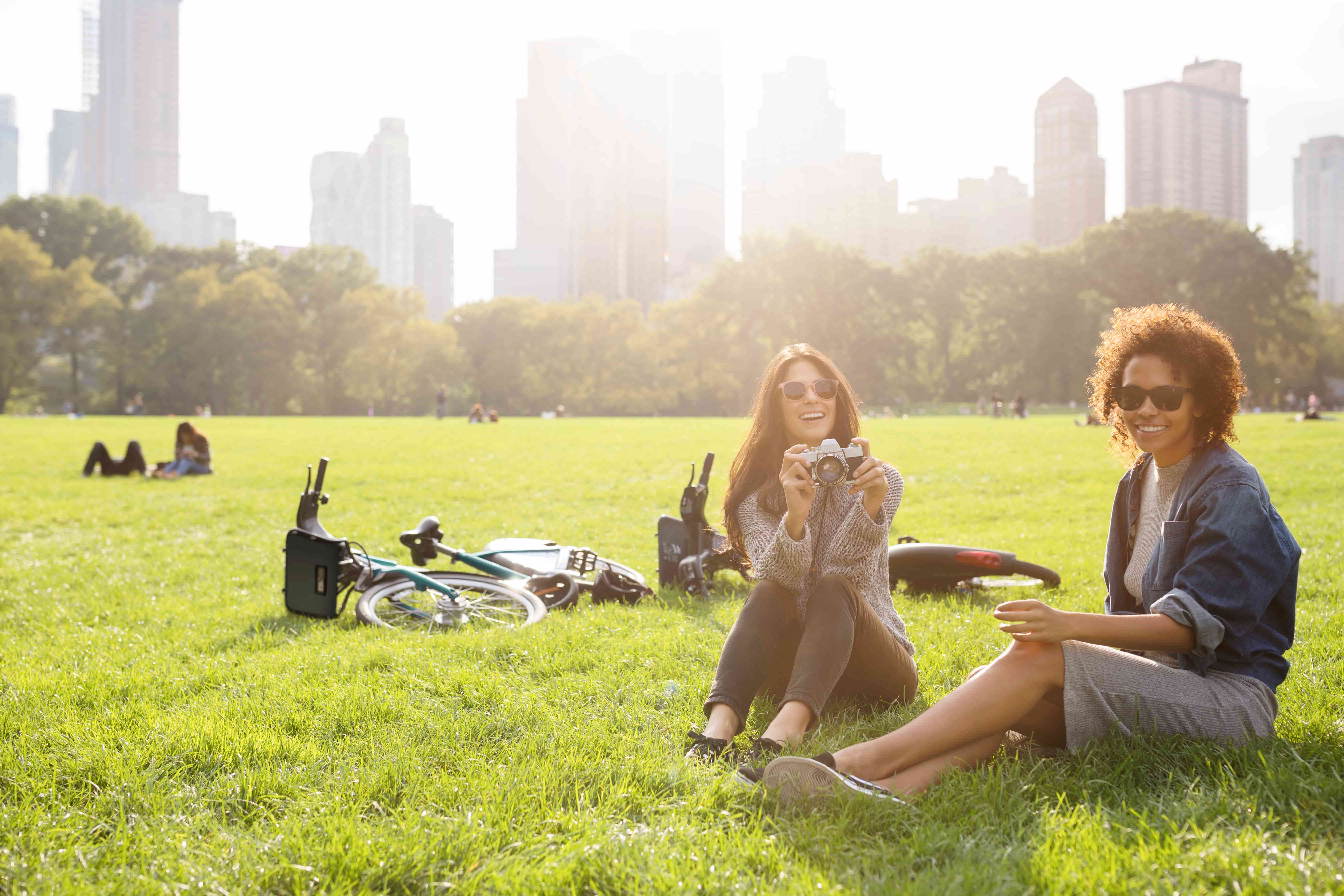 Happy woman holding camera while relaxing with friend on grassy field