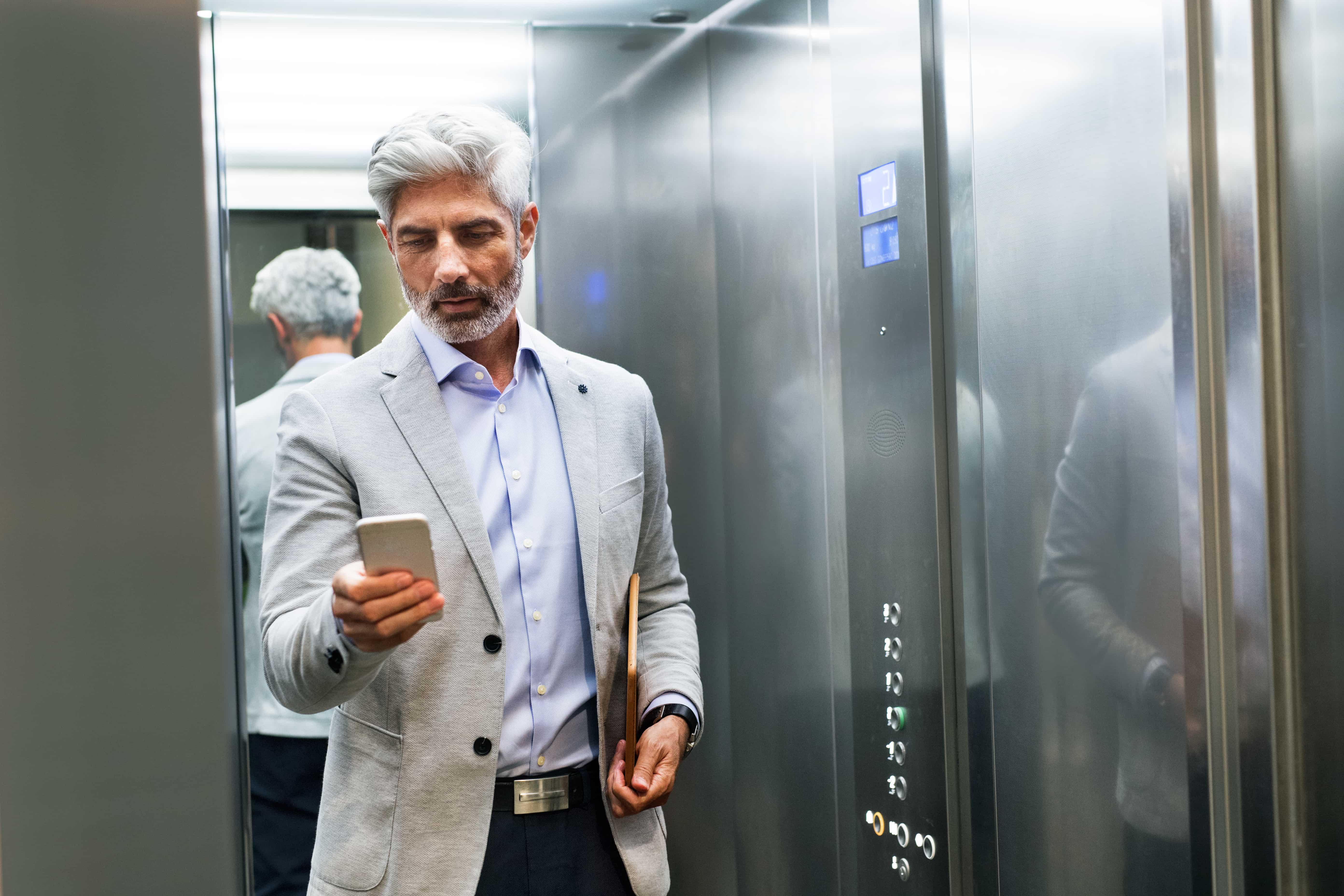 Mature businessman with smartphone in the elevator